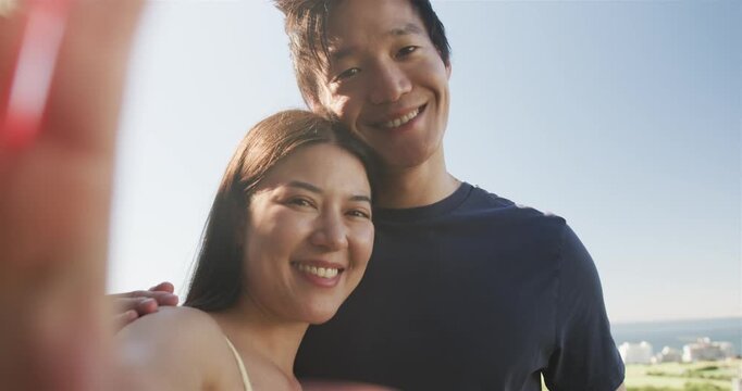 Diverse couple smiling at ocean view, man in navy tee leaning, woman holding phone, finger entering