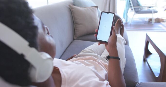 Man reclining on sofa at home wearing headset, tapping smartphone trying to reload content spinner