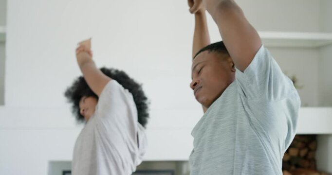 African American couple on cue, clasping hands, sidebending to stretch by fireplace, ending smiling