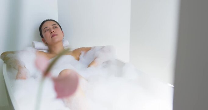 Camera shifting is moving pink calla flowers into frame while woman is lying in bathtub, resting