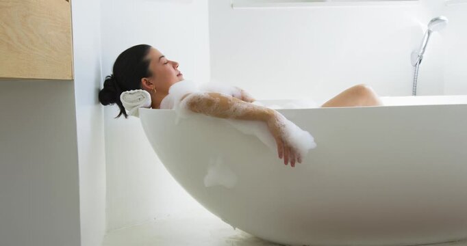 After settling into freestanding tub, woman is slowly sliding forearm and brushing foam for comfort