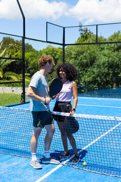 Couple playing on blue padel court in sportswear holding black rackets with yellow ball near net