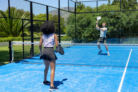 Male and female opponents holding paddles on blue court near net, wearing sportswear hitting ball