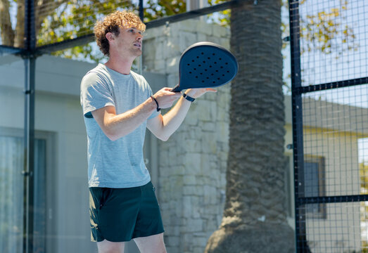 Man holding padel racket and tracking incoming ball on outdoor court, preparing to return