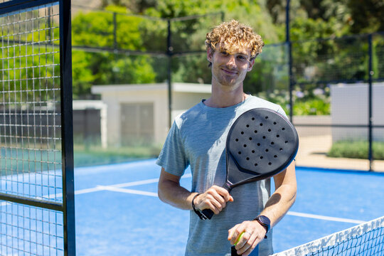 Man in sportswear standing on blue padel court holding racket and ball, beginning serve to play