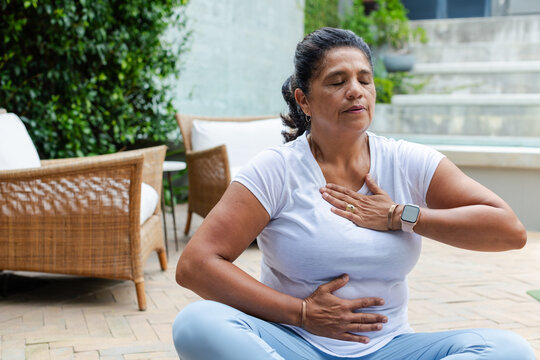 Mature African woman sitting cross-legged on patio meditating, wearing white tee and smartwatch