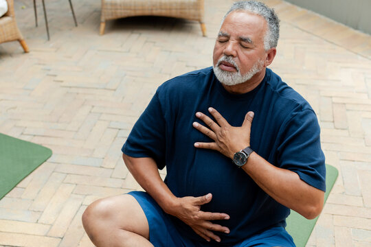 Senior African American man meditating on green mat on herringbone patio wearing navy tee and watch