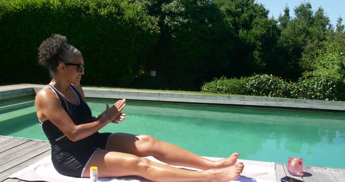 African American woman grabbing sunscreen, rubbing legs by pool for sun protection, copy space
