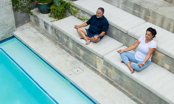 African couple in activewear sitting meditating on cushioned steps by pool near drainage grate