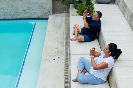 Mature couple sitting on bench poolside in activewear, pressing hands by access cover, copy space