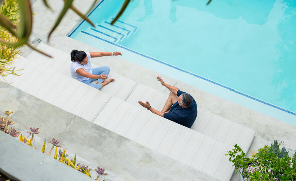 African American senior couple sitting on pool steps beside turquoise water wearing bracelets watch