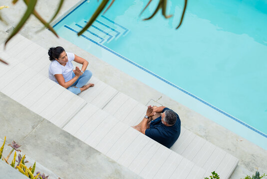 Mature African couple sitting on white bench beside tiled pool steps, pressing palms, wristwatch