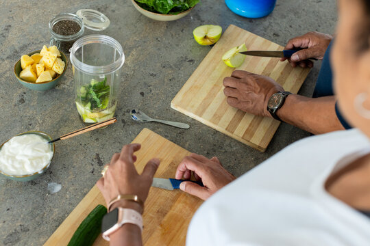 African American couple chopping cucumber and slicing apple on cutting boards at home with blender