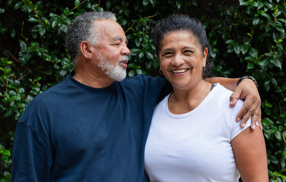 Senior African American couple standing close, posing for portrait by hedge with navy shirt, watch