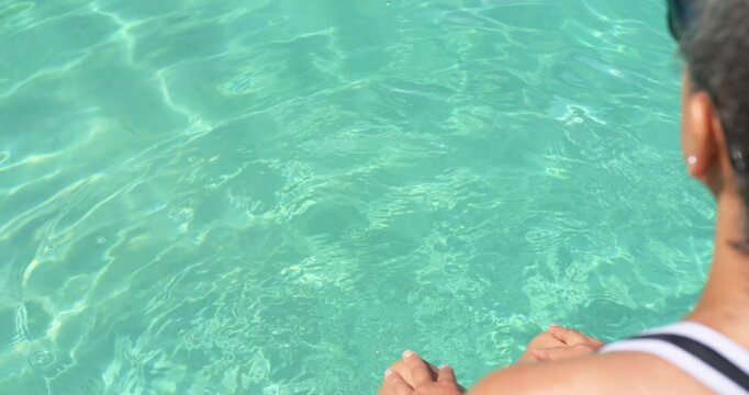 African American woman sitting dock dipping foot into blue water, relaxing in swim top, copy space