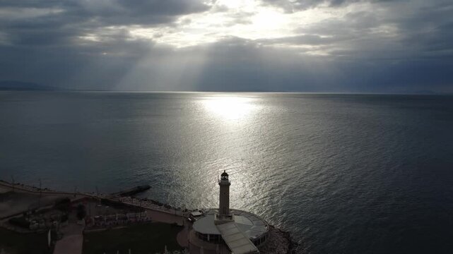 Aerial view of a stone lighthouse on a pier under a dramatic cloudy sky