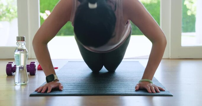 African American woman in leggings performing knee push-ups on mat at home, checking smartwatch