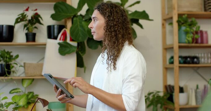 Non-binary adult after checking tablet, tapping and inspecting plants at plant shop, updating stock