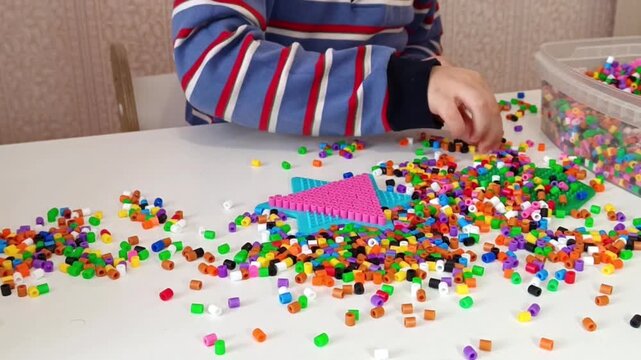 Close-up of a child's hands placing colorful plastic fusebeads onto a pegboard to form a pattern. This activity supports fine motor skill developmentin early childhood.