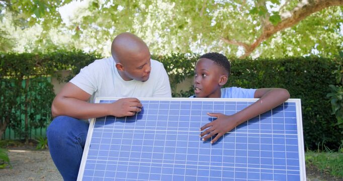 African American dad and teen son checking solar panel in garden, boy tapping cells sparking lesson