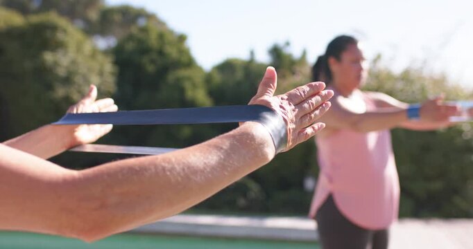Diverse women stretching resistance band on pool deck following pink-top woman leading for fitness