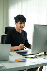 Fototapeta premium asian Graphic designer man drawing on graphic tablet with stylus. designer or digital artist at work while working at his creative workplace in the modern office