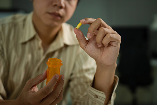 close up of male employee holding pills from bottle while sitting by desk in office