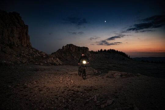 Man mountain biking at night with headlight on rocky terrain