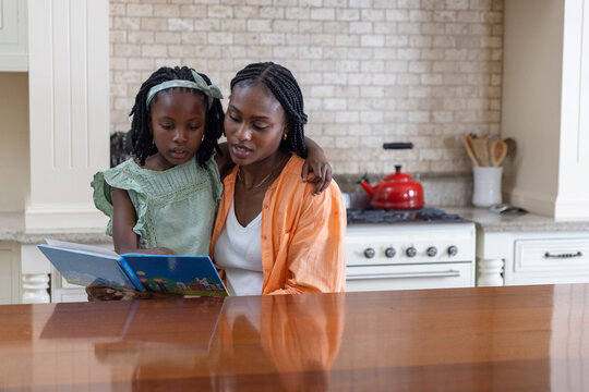 African American mother and child reading blue book at kitchen counter with red kettle