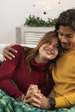 Diverse couple on sofa at home leaning together holding hands over green blanket with smartwatch