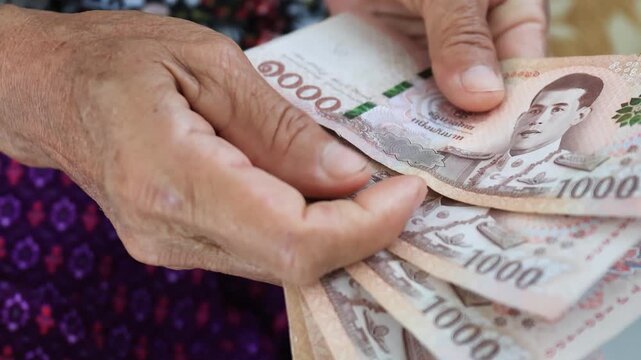 Elderly hands counting Thai banknotes Baht, Money close-up. Concept of retirement savings, pension income, financial security, budgeting, and senior financial planning