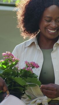 Vertical video: Mother watering pink plant in garden after hand with can, caring, wearing beige top