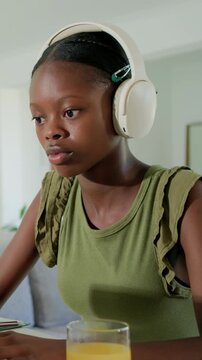 Vertical video: Phone pinging, teen typing at home table in green top with laptop, headset, juice