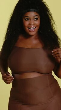 Vertical video: Camera starting close-up, woman model adjusting brown two-piece as posing in studio