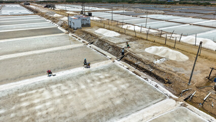 Naklejka premium Salt pans with workers harvesting sea salt in evaporation ponds aerial view
