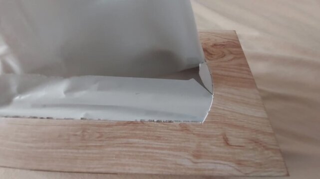 Hand pulling out white paper tissue from wooden box dispenser