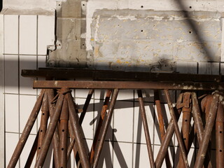 Naklejka premium several rusted steel construction props leaning against a wall during a renovation. The background features a section of white square tiles and a rough grey concrete patch where tiling has been remove