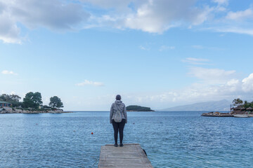 Fototapeta premium One person standing at the end of a wooden pier in the water on a beach at Adriatic sea coast in Ksamil, Saranda, Albania