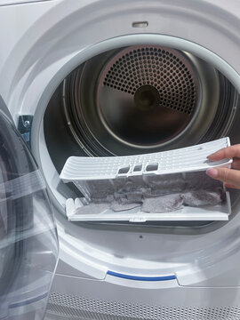 close up female hand taking lint out from dirty air filter of dryer machine after drying. cleaning Dirty filter. hair, wool from the filter in hand. Front Load Tumble Laundry electric Dryer Machine.