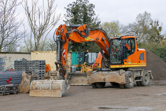 Nancy, France - March 29th 2026 : View on an orange wheeled excavator Liebherr A 918 Compact Litronic on a construction site with construction equipment and trees in the background.