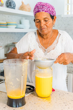 Caribbean woman straining fresh tropical juice in kitchen