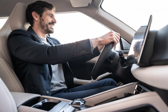 Smiling businessman driving modern car with touchscreen