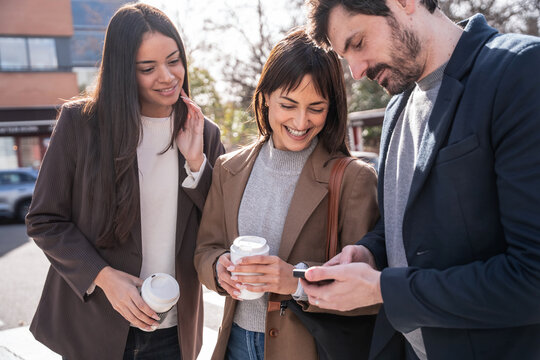 Business colleagues on coffee break checking phone outdoors