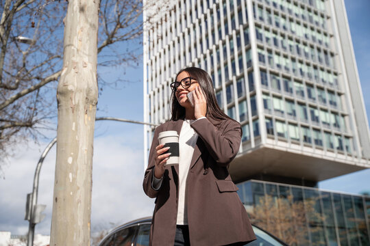 Businesswoman on phone with coffee near modern office