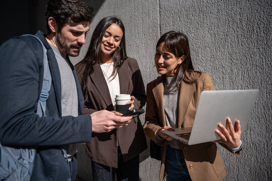 Business colleagues reviewing smartphone and laptop outdoors