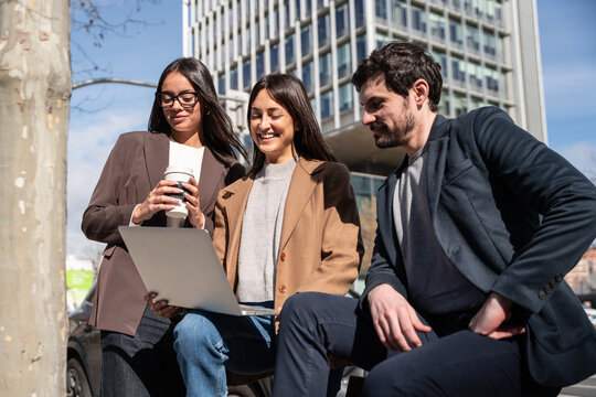 Business team reviewing laptop outdoors near office building