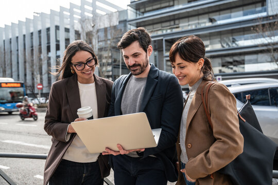 Business colleagues reviewing laptop outdoors in urban setting