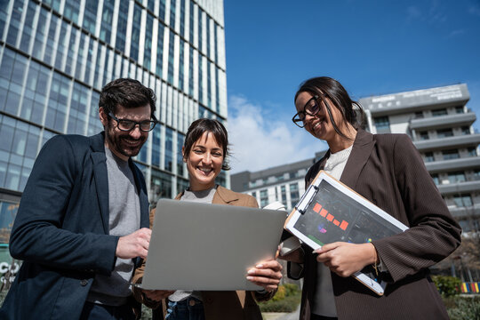 Business team meeting outdoors, reviewing laptop and report