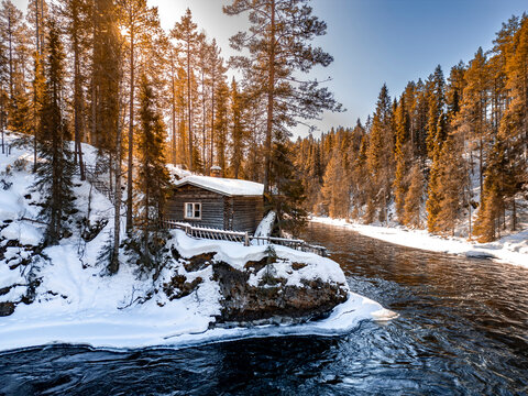 Snowy riverside cabin in Finnish forest at sunrise
