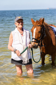 smiling teen age girl posing with horse at edge of ocean